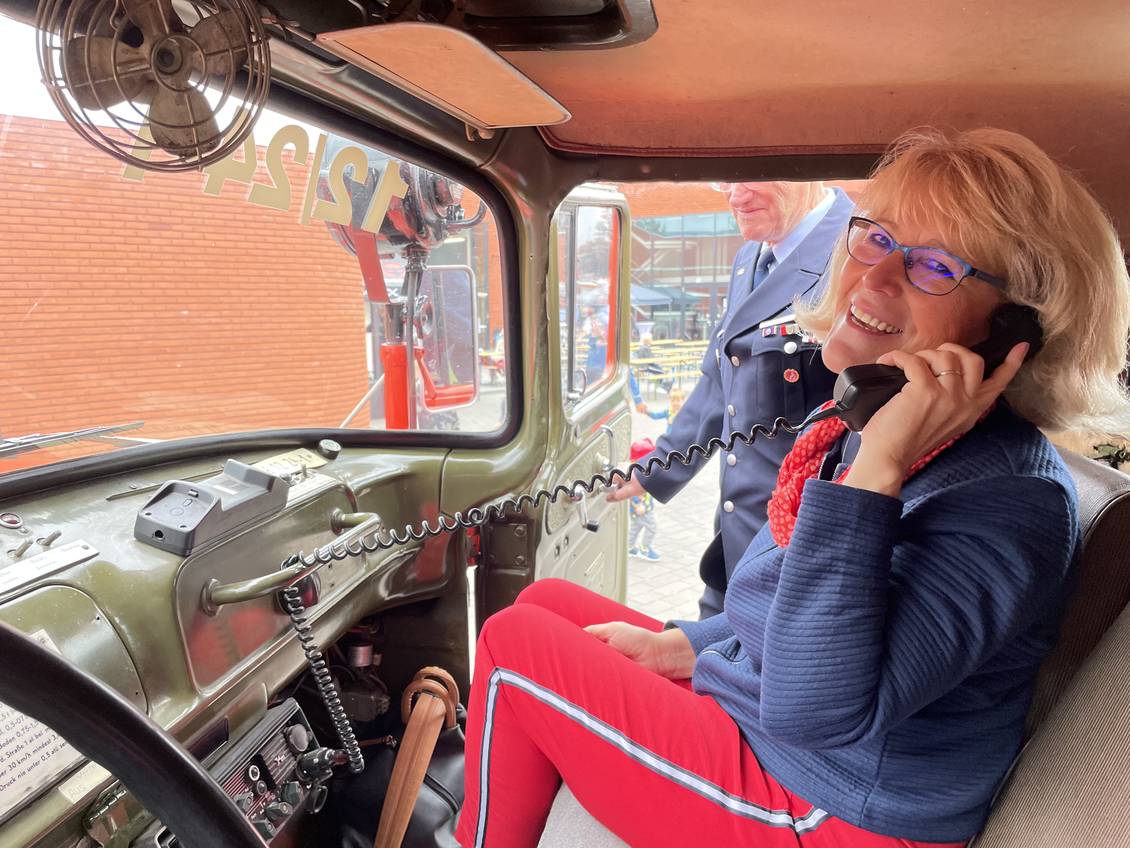 Das Foto zeigt eine Frau, die sich in einem Feuerwehrfahrzeug einen Telefonhörer ans Ohr hält.