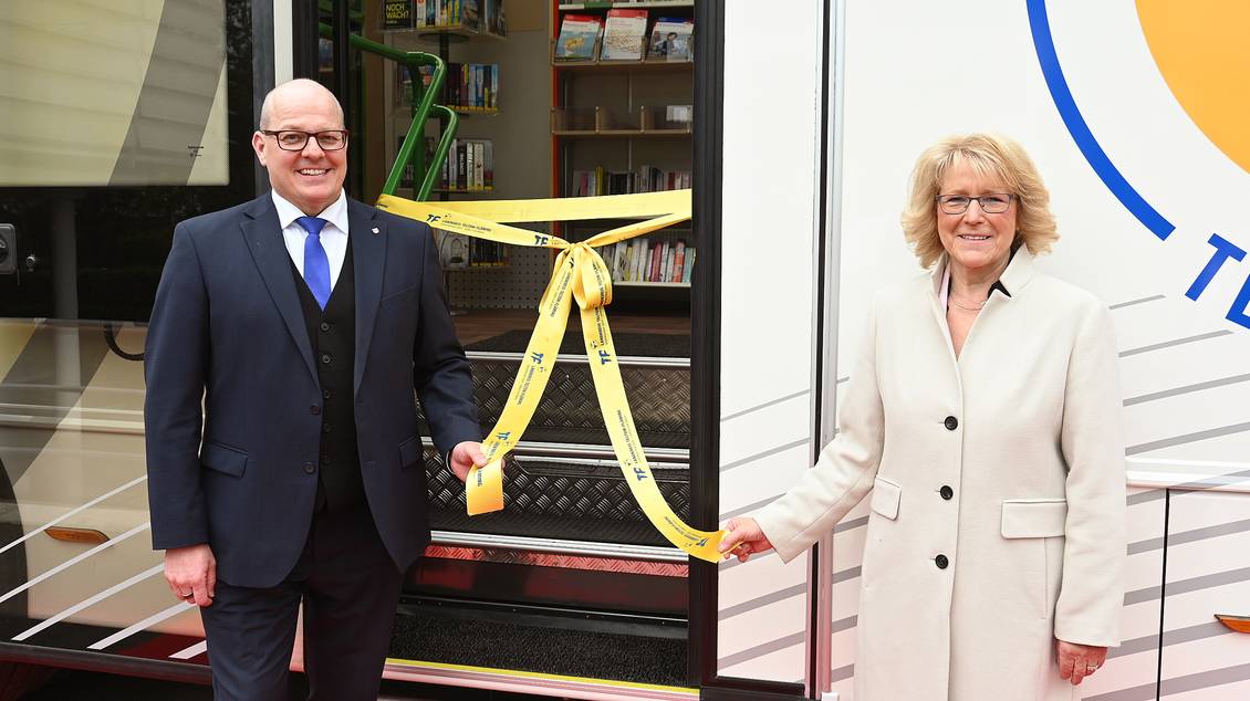 Das Foto zeigt zwei Personen beim Öffnen einer Schleife vor der Tür der neuen Fahrbibliothek.