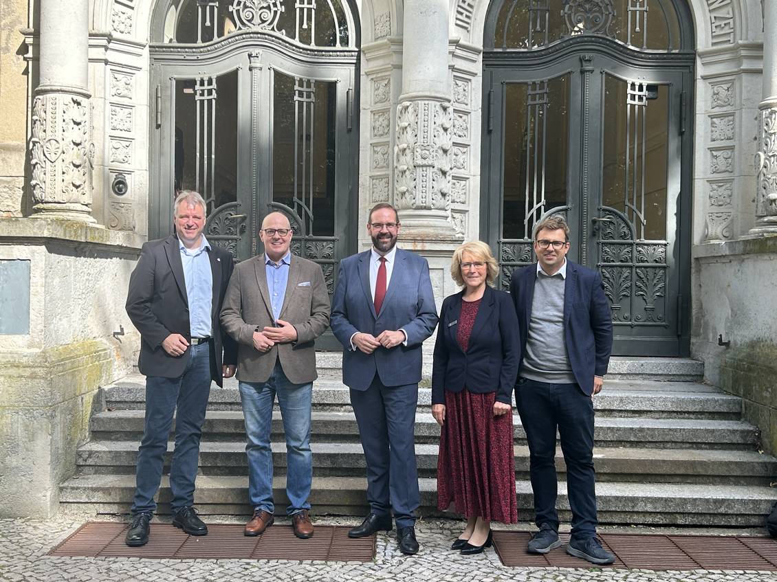 Das Foto zeigt fünf Personen vor dem Eingangsportal des Altbaus des Gymnasiums. 