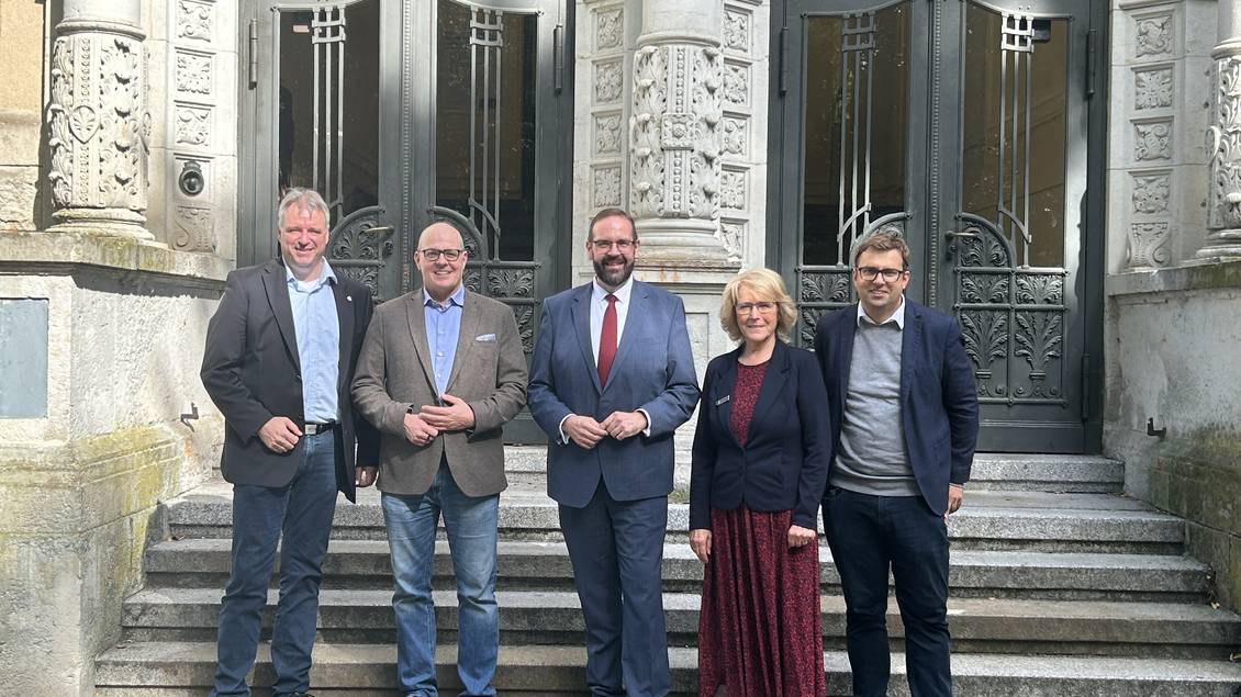 Das Foto zeigt fünf Personen vor dem Eingangsportal des Altbaus des Gymnasiums. 