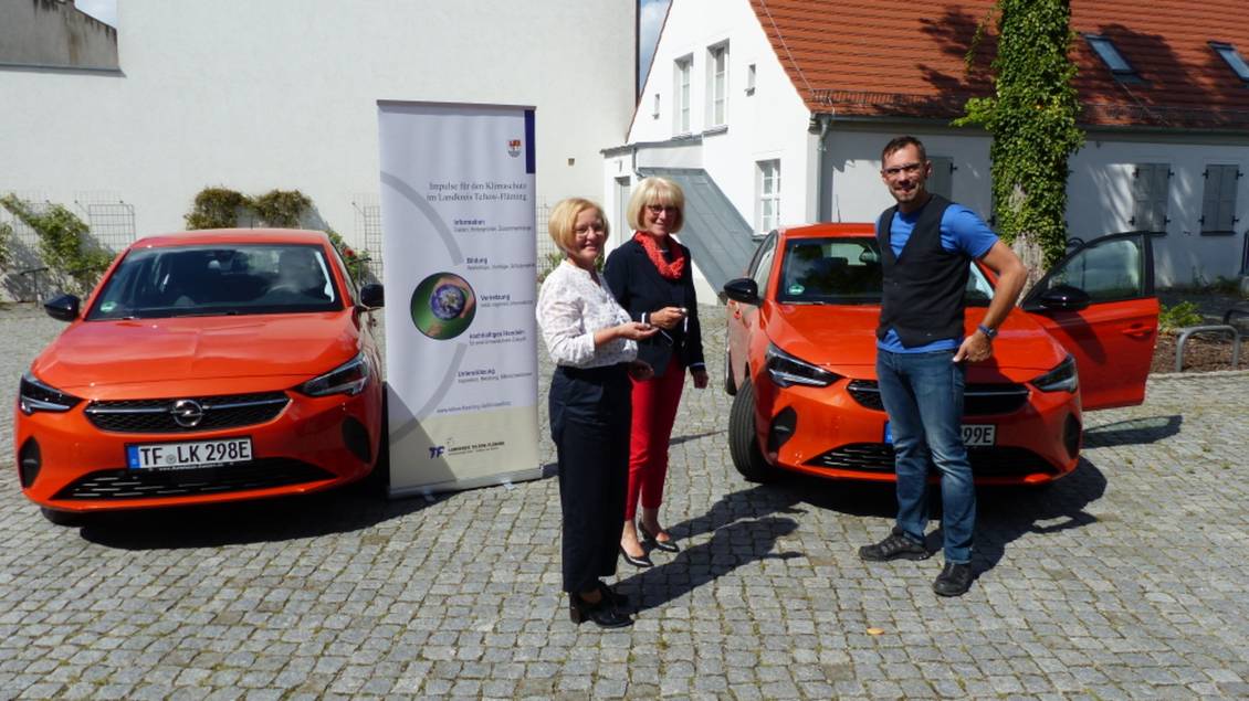 Das Foto zeigt eine Gruppe von Personen vor zwei roten PKW.