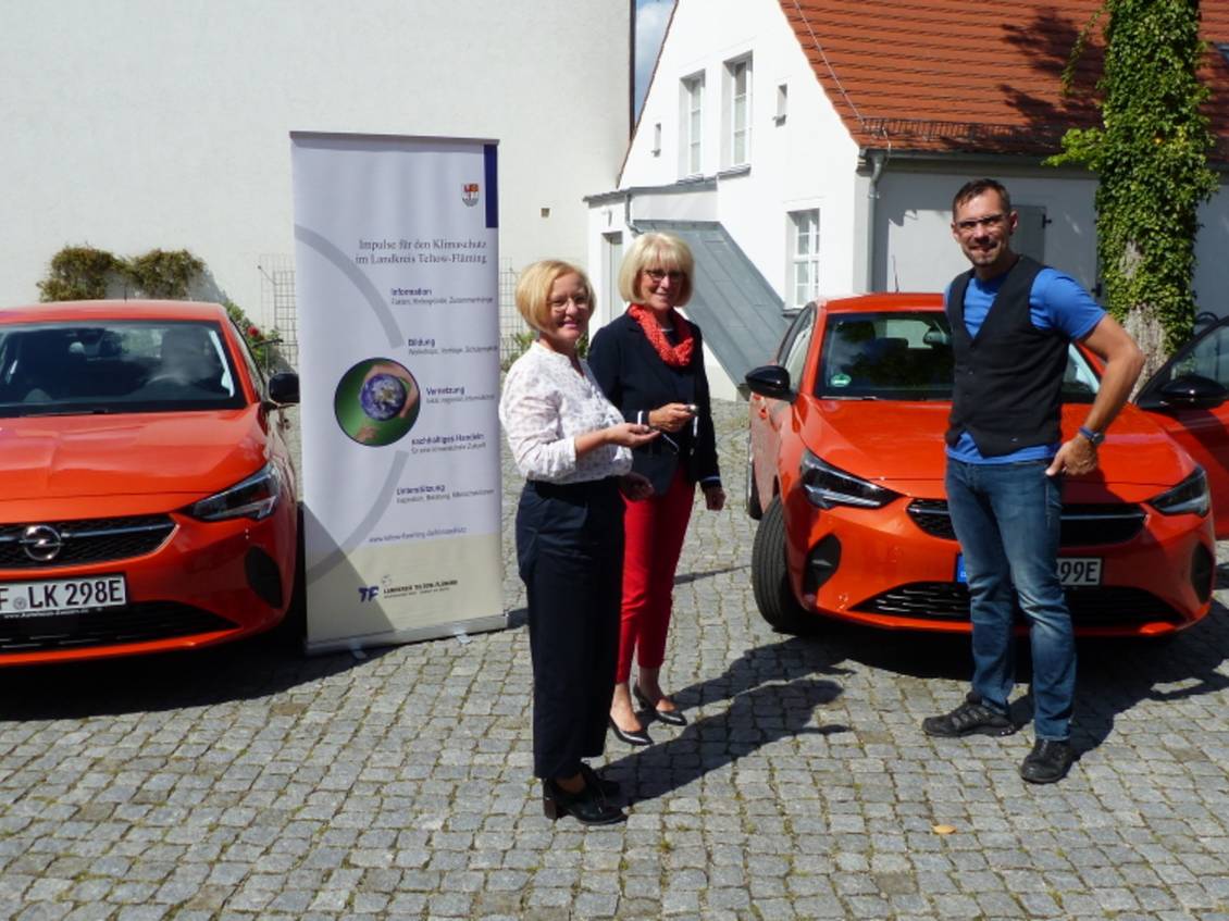 Das Foto zeigt eine Gruppe von Personen vor zwei roten PKW.