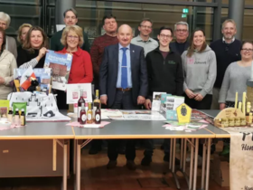 Das Foto zeigt eien Gruppe von Menschen, die um einen Tisch stehen. Auf dem Tisch finden sich unterschiedliche Produkte.