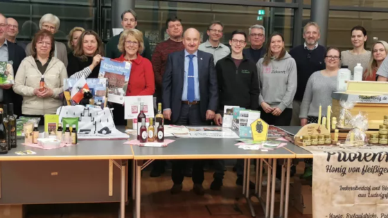 Das Foto zeigt eien Gruppe von Menschen, die um einen Tisch stehen. Auf dem Tisch finden sich unterschiedliche Produkte.